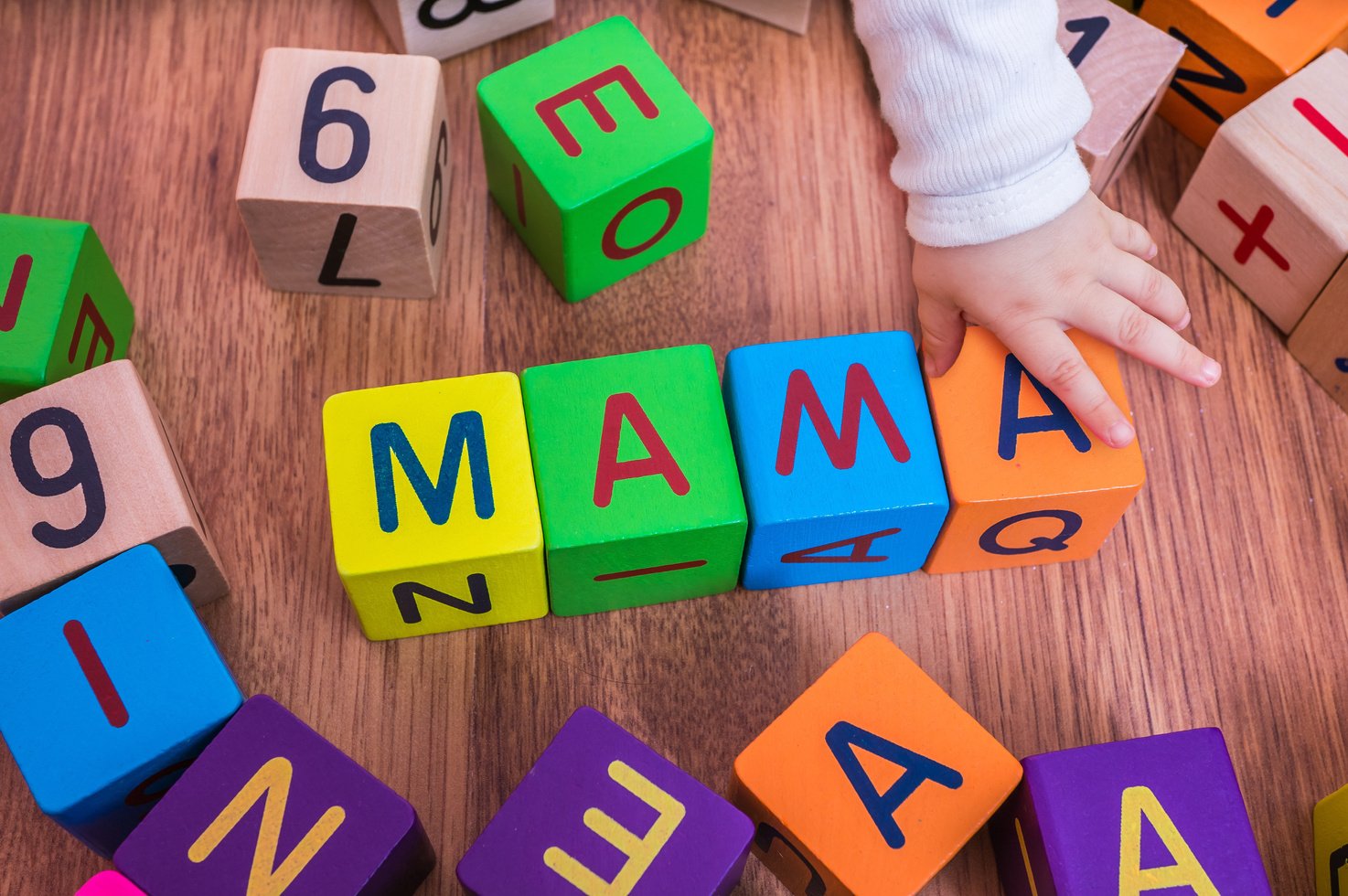 Baby is playing with colorful cubes and writting Mama.